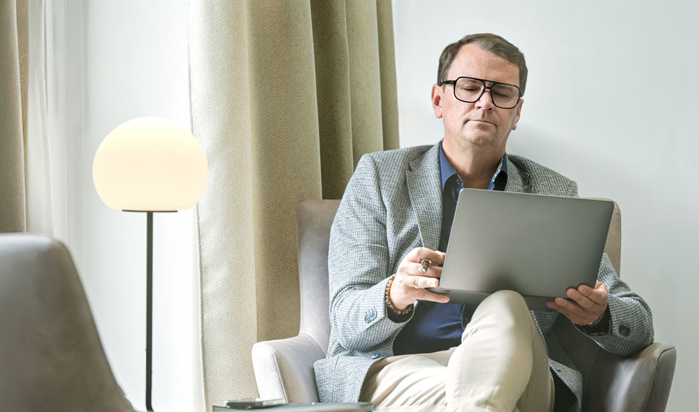 Porträt von Markus Baumeister, sitzend mit geöffnetem Laptop am Knie.